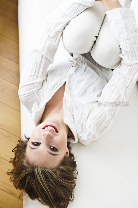 穿着白衬衫的微笑模特躺在沙发上，抱着膝盖