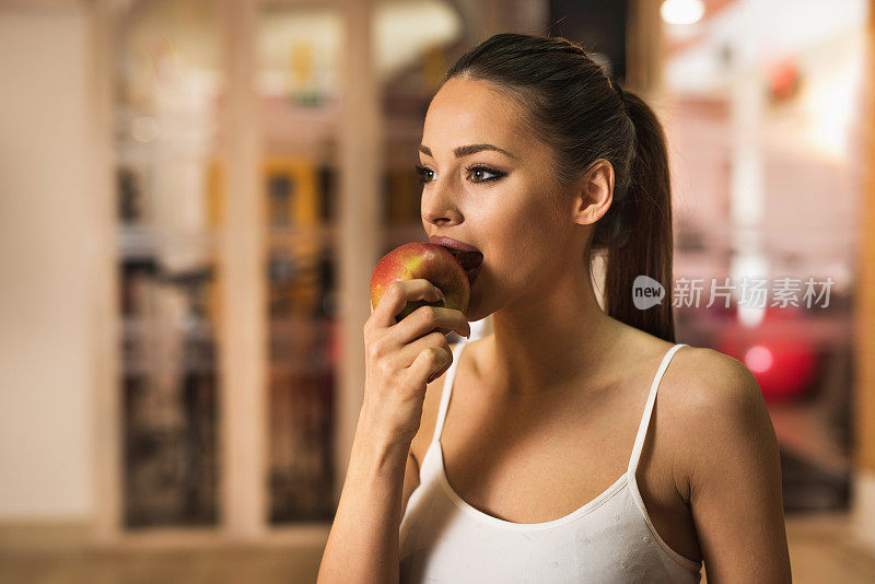 年轻女运动员在健身俱乐部咬苹果。