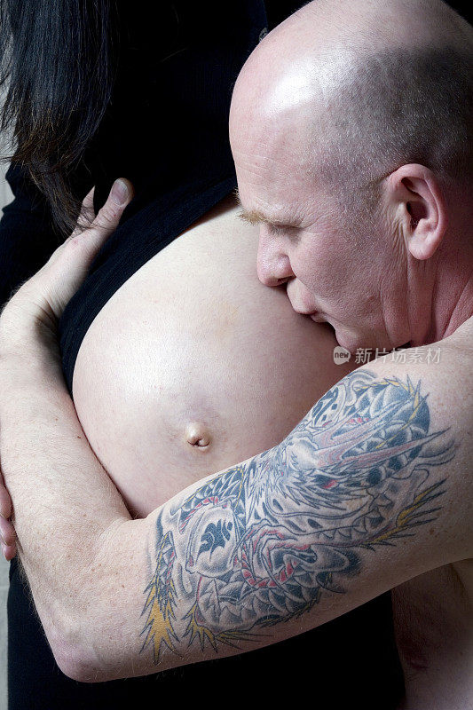有纹身的父亲亲吻他怀孕妻子的肚子。