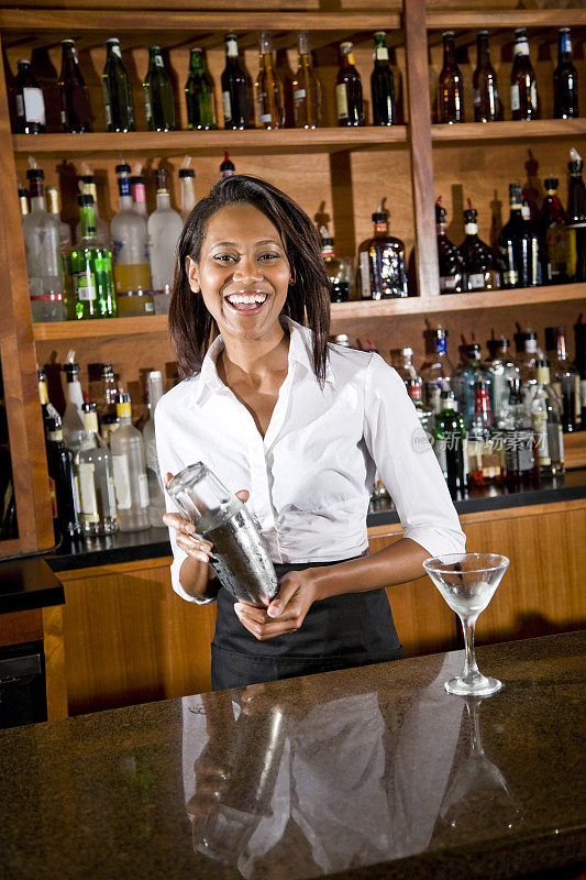 快乐的非裔美国女调酒师在吧台后面调酒