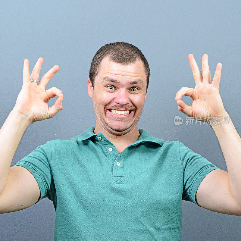 一个男人在灰色背景下竖起大拇指或ok手势的肖像
