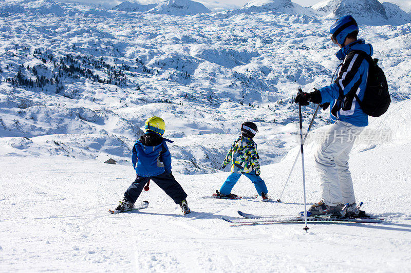 一个阳光明媚的日子，父亲和两个男孩在奥地利度假胜地的山顶滑雪