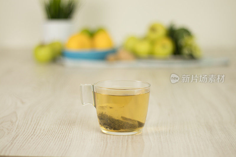 白色木桌上的茶杯上有模糊的水果背景。茶准备原料。
