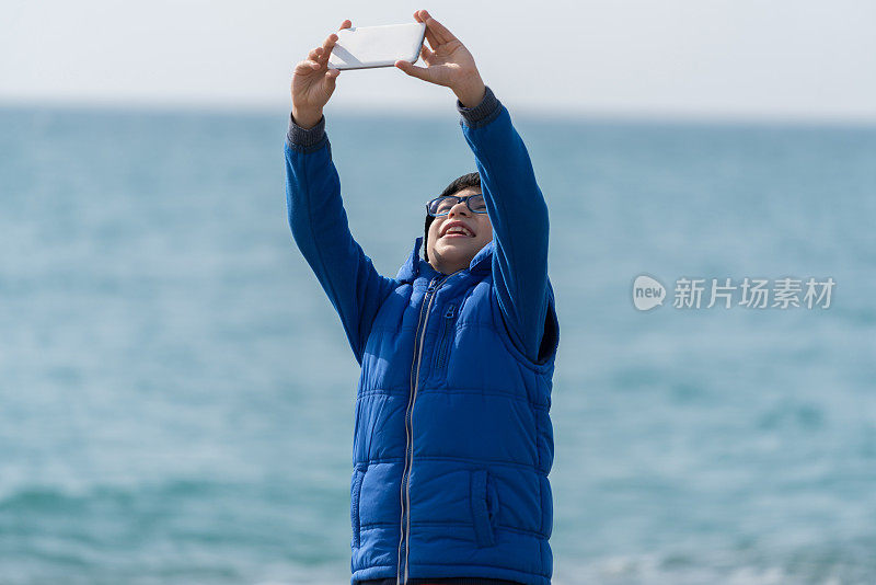 快乐男孩在海滩上散步，用手机自拍