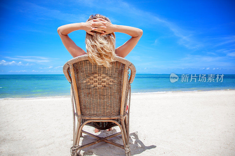 一个戴着帽子的金发女人坐在椅子上，看着美丽的海景