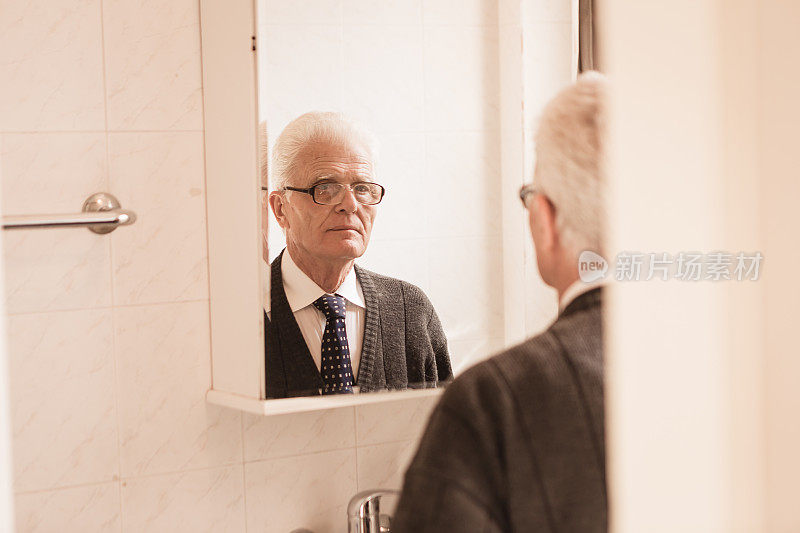 老年人在家里。老男人看着浴室镜子，系着领带