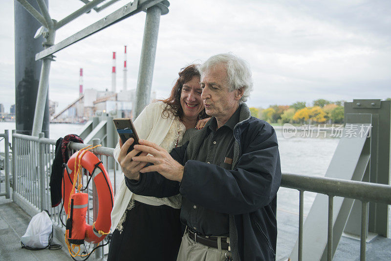 这对老年夫妇正在纽约曼哈顿旅行。在罗斯福岛等渡船，用智能手机自拍