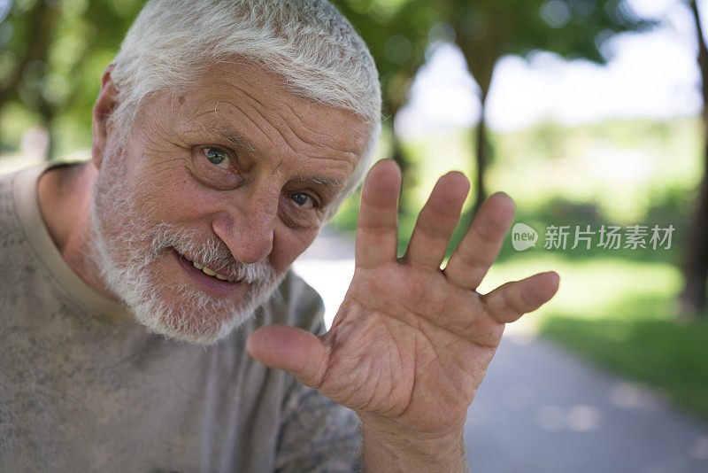 在模糊的公园背景上微笑的高级好看和移动的手向前的肖像