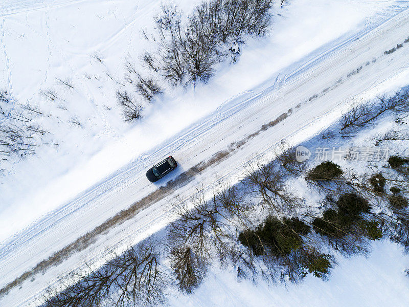 一辆汽车在冬季道路上的鸟瞰图。冬天的乡村景观。空中拍摄的雪域森林与一辆汽车在道路上。无人机从上面拍下的。航拍照片。四轴飞行器。