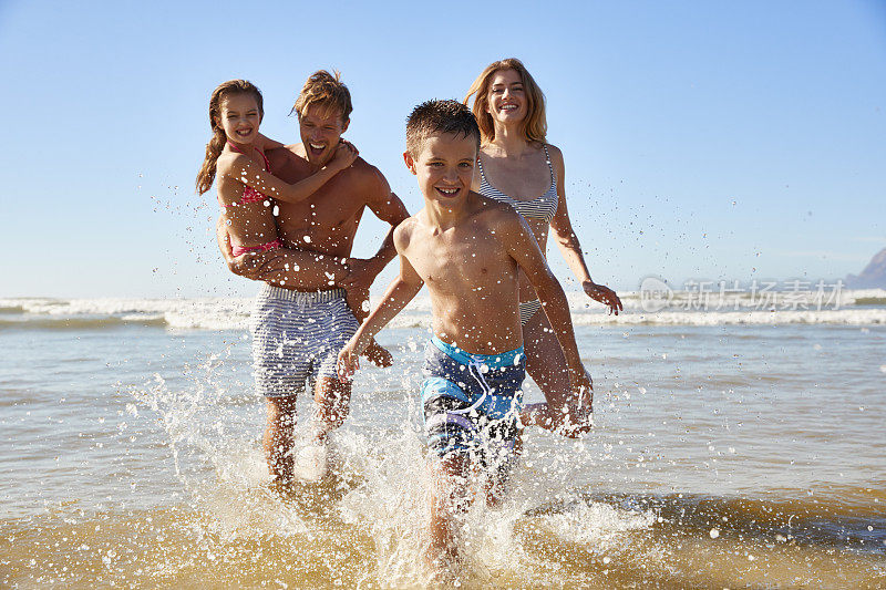 一家人在夏天的海滩度假跑出大海对着相机