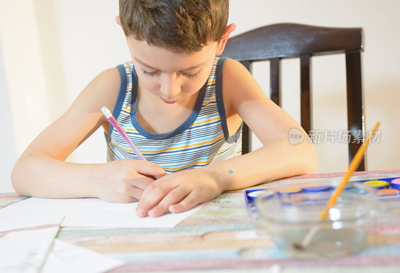 男孩正在用水彩和彩色蜡笔画画。