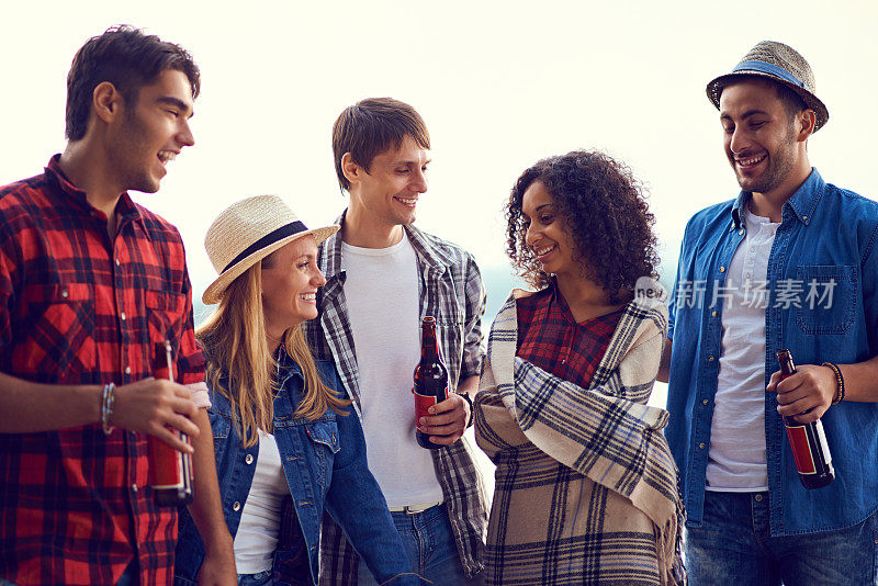 快乐积极的年轻的多民族朋友喝啤酒和聊天，同时放松在户外露营