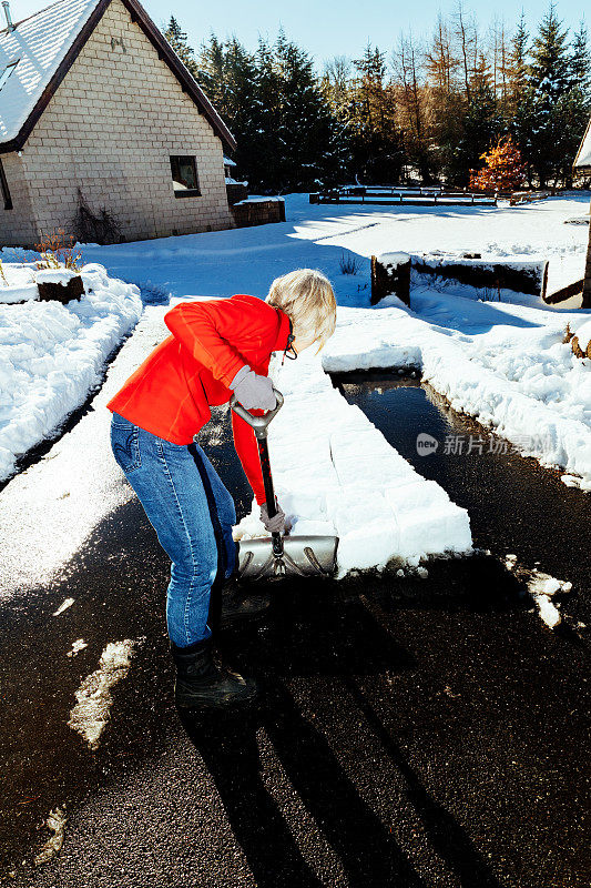 老妇人正在用雪铲清理积雪