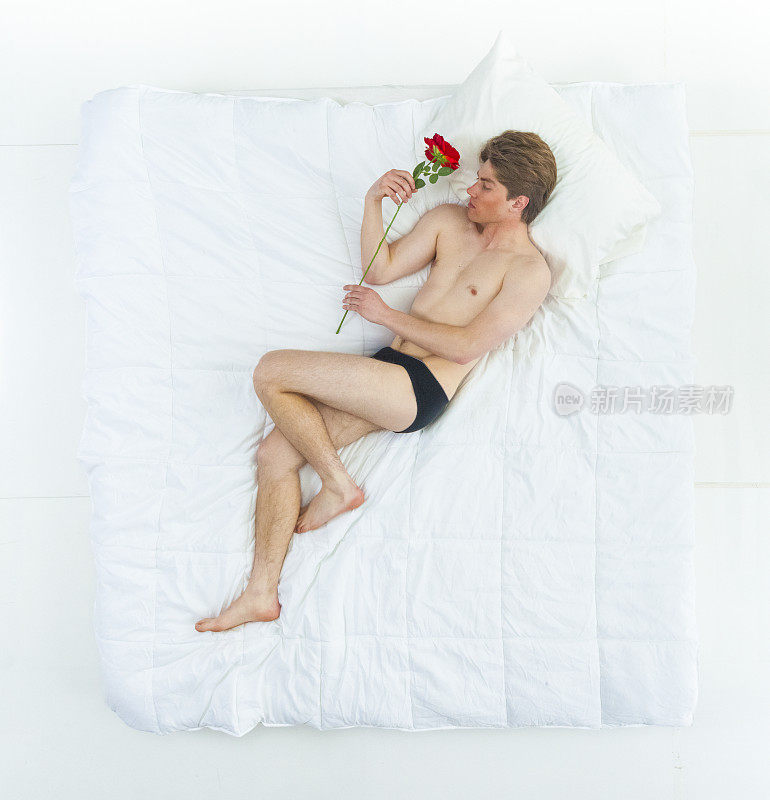 性感的男人在床上穿着内裤，拿着一朵玫瑰