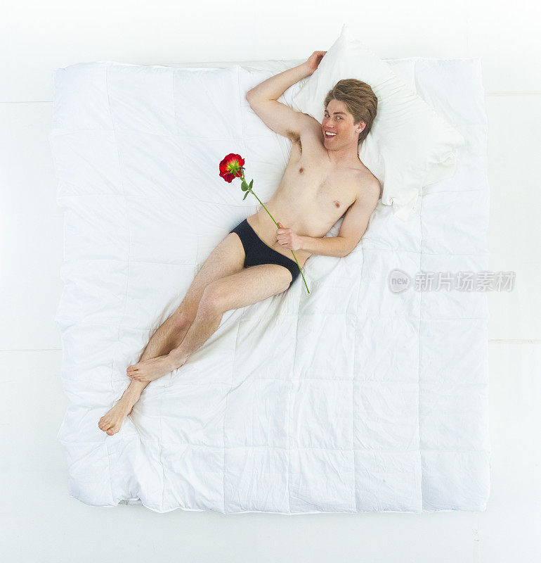 性感的男人在床上穿着内裤，拿着一朵玫瑰