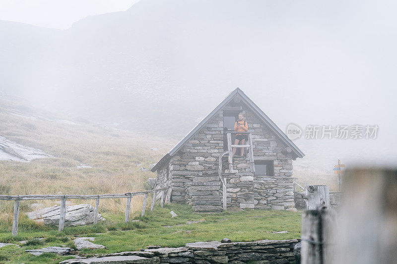 徒步者站在山草地上的石屋台阶上