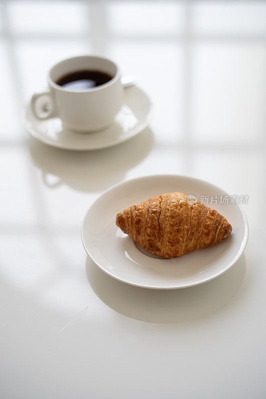 白杯子里装着牛角面包和黑咖啡，大理石桌上放着茶托