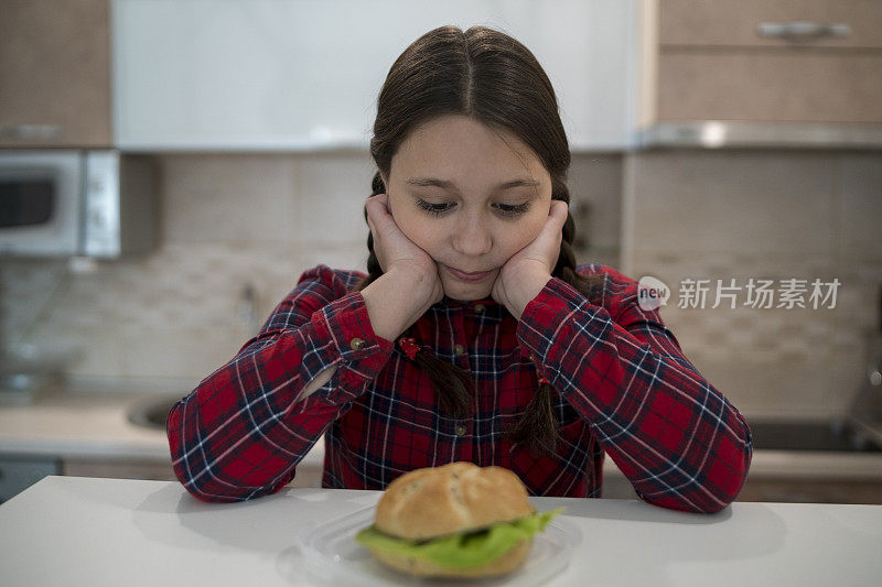 十几岁的女孩看着开胃的汉堡躺在她面前的桌子上