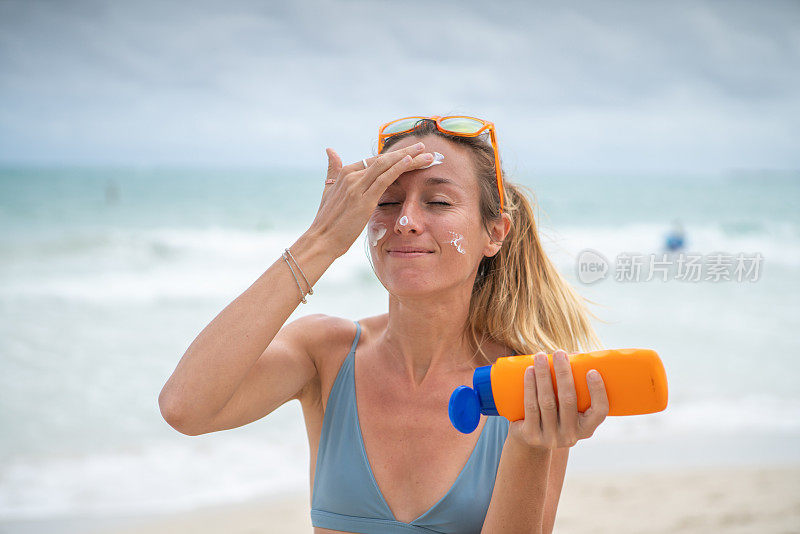 夏日——年轻女子在海滩上涂抹防晒霜，保护皮肤