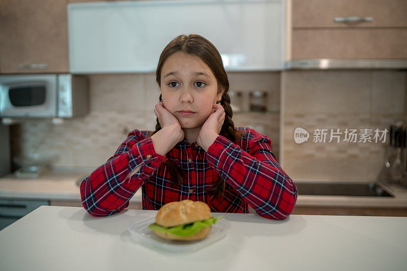 十几岁的女孩看着开胃的汉堡躺在她面前的桌子上