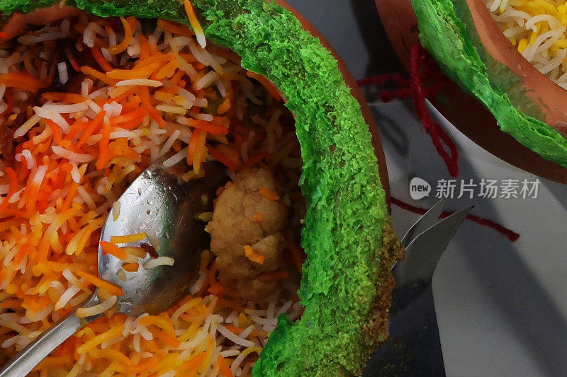 近距离的图像赤陶罐与金属勺子包含印度外卖米饭，鸡肉biryani与鸡masala肉汁酱在玻璃桌上
