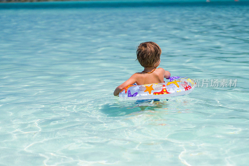小男孩与充气环在海上游泳的后视图。
