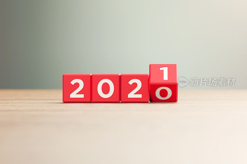 “2020”和“2021”书写的红木块坐在前面的木头表面上，背景散焦