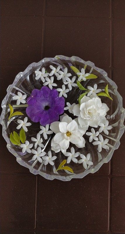 白色的茉莉花，白色的山茶花和紫色的矮牵牛花装饰在装满水的水晶盘里