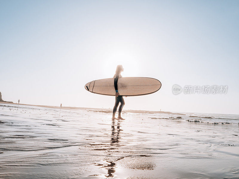 清晨，一位女子在沙滩上用冲浪板观看海浪