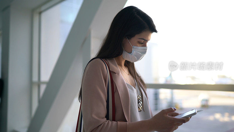 年轻女旅客在机场使用手机-戴口罩