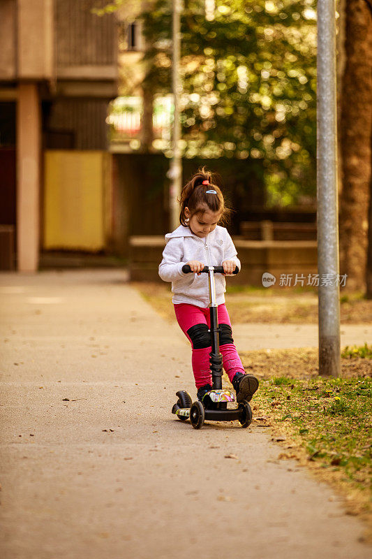 可爱的小女孩骑着滑板车在街上