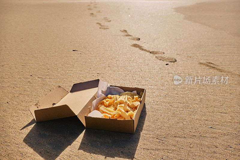 在一个阳光明媚的秋日，康沃尔纽基托万海滩的沙滩上放着一盒炸鱼薯条。