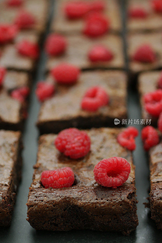 深灰色背景上自制的巧克力和覆盆子布朗尼方块，上面是覆盆子，聚焦前景