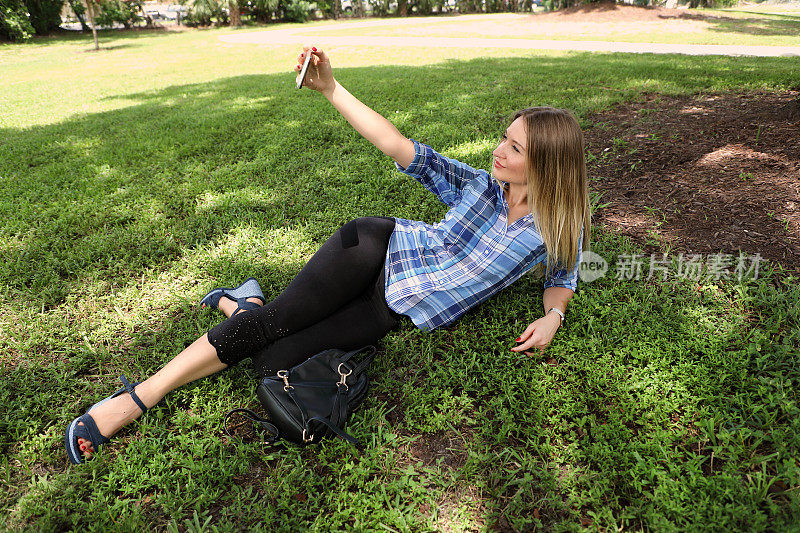 美丽年轻的成年女子与手机在绿色的草地上