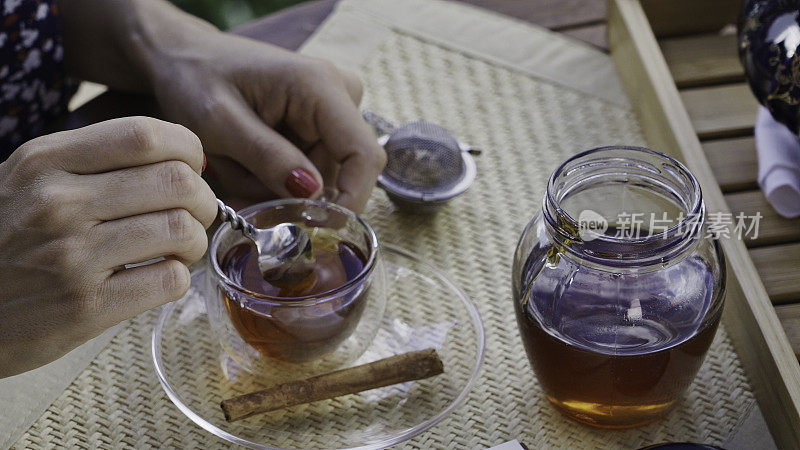 近距离观察年轻女子的手倒蜂蜜天然甜味剂热茶杯在一张桌子上的户外露台