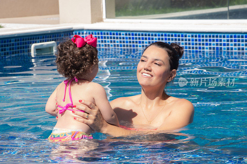 在一个阳光明媚的夏日，妈妈和小女儿在游泳池里玩耍
