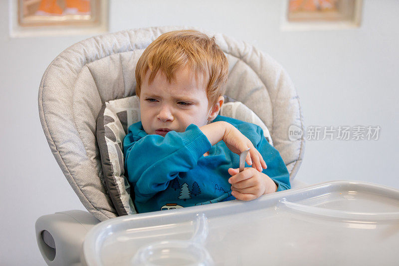 金发小男孩坐在喂食椅上做鬼脸拒绝进食