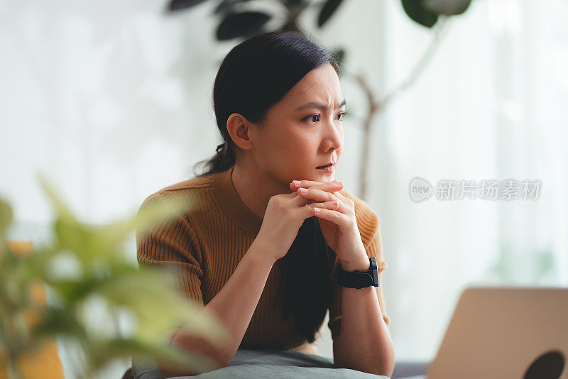 亚洲女性坐在沙发上，担心银行票据、抵押贷款债务和生活成本的账单支付问题。