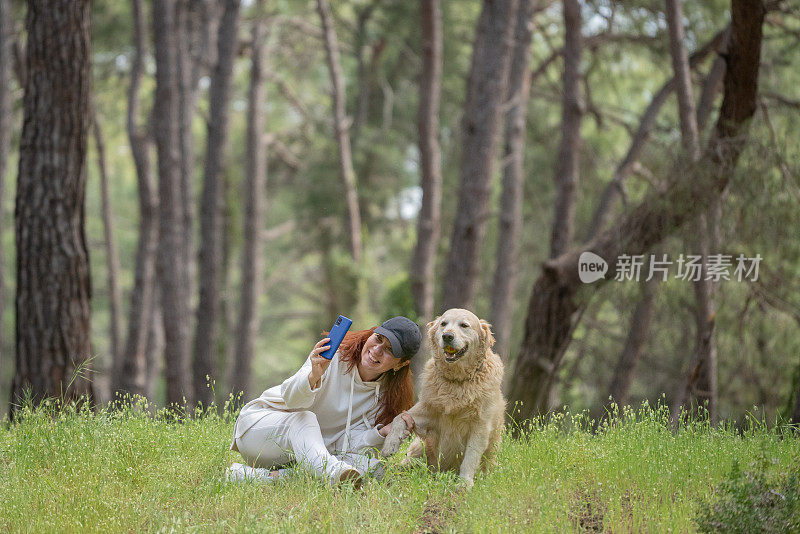 美女和她的金毛猎犬坐在草地上想自拍