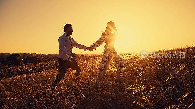 夕阳下的风景有一对恋人，一男一女。夏天美丽的大自然。在风中生长的草的天然小穗。