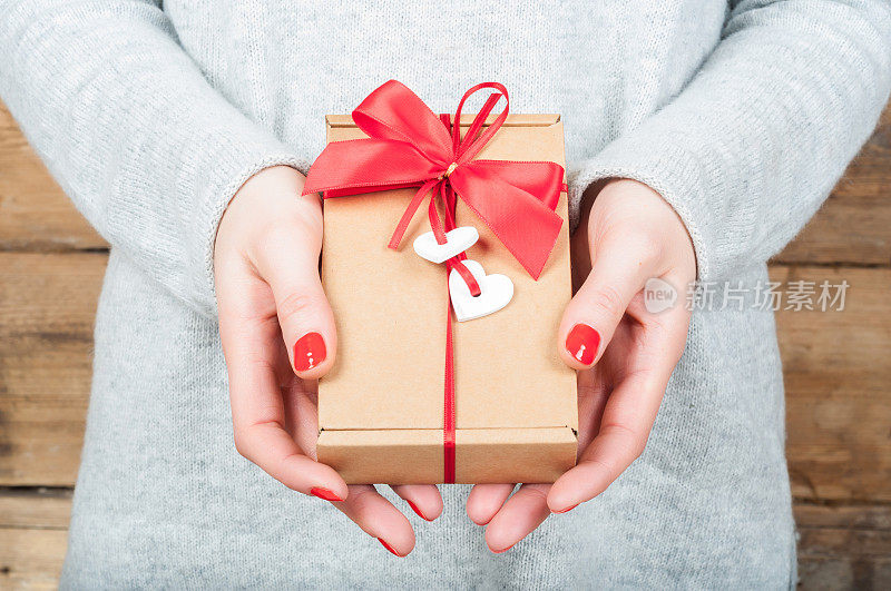 手握礼物在牛皮纸盒上的木制背景