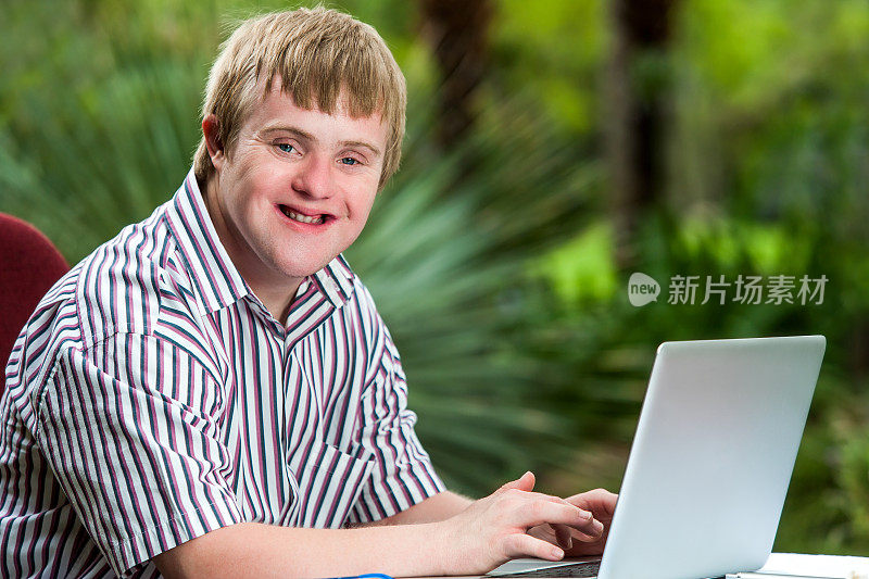 一个在花园里用笔记本电脑打字的残疾年轻人。