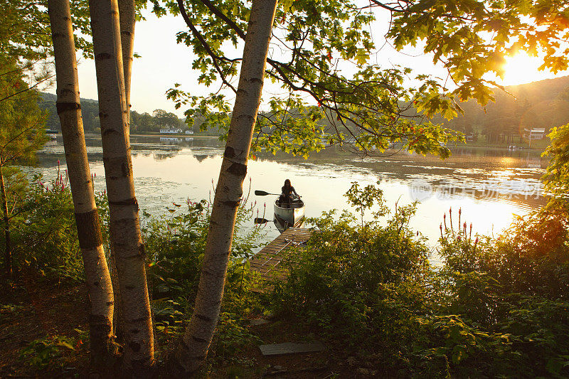 年轻女孩划着独木舟与明亮的日出和树木
