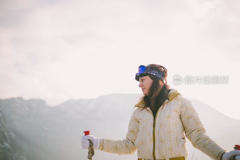 近景美丽的年轻女子在冬天的衣服站在一边，手拿木棍的背景雪山