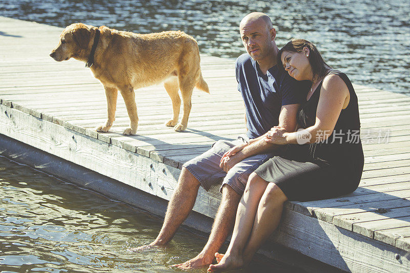 一对年轻夫妇和一只狗坐在湖边的码头上。