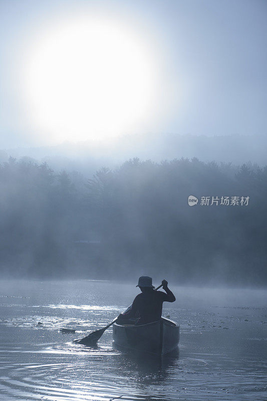 户外女孩在薄雾日出的湖上划独木舟背光