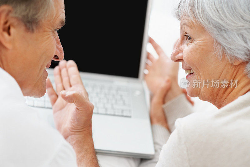 一对老年夫妇一边用笔记本电脑一边看着对方
