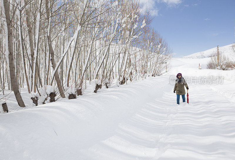 女人撑着红伞走在雪道上