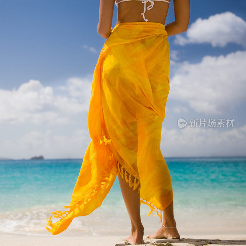 光着脚的女人裹着纱笼站在加勒比海滩上