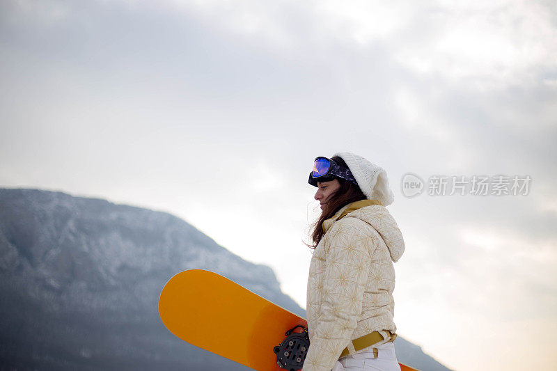 女人拿着滑雪板，背景是高山